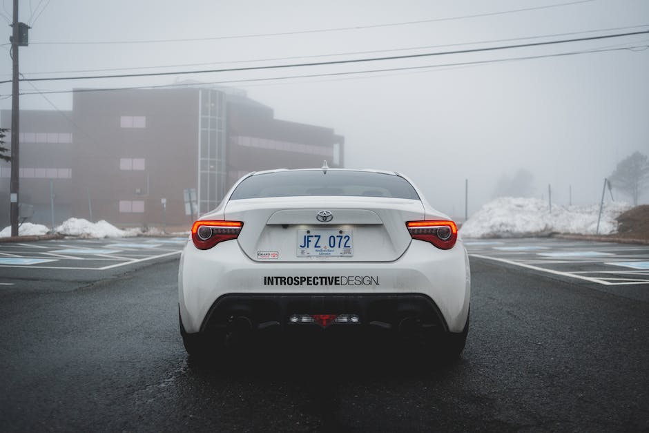 A car with headlights on, driving on a foggy and snowy road.
